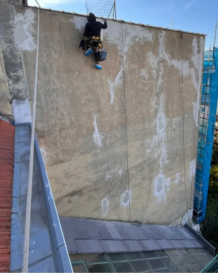 Cordiste au travail sur un mur pignon dont le cimentage est décollé par plaques