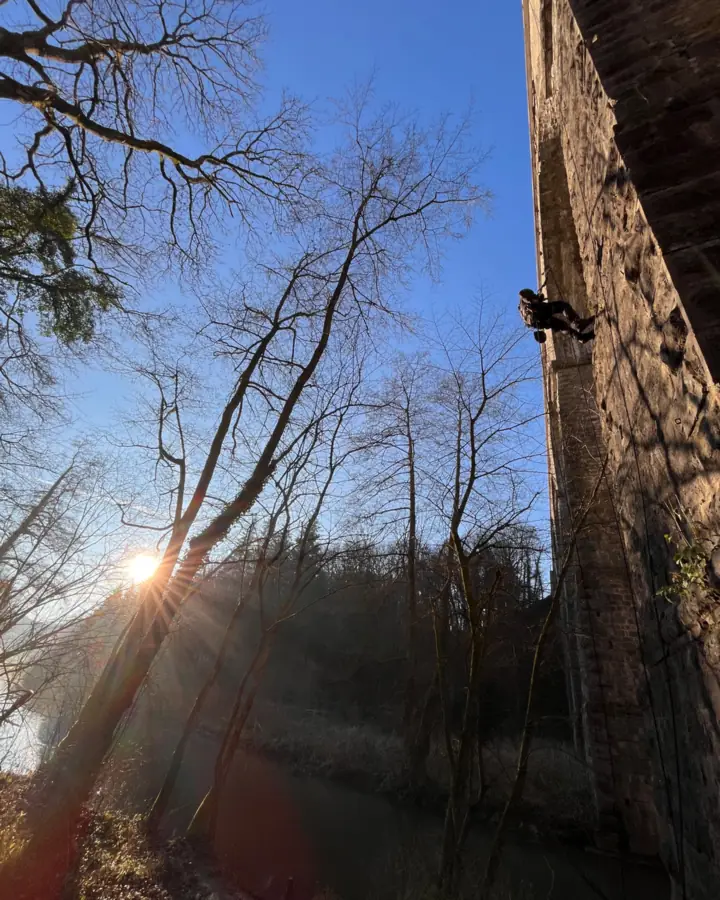 Cordiste en descente le long de la pile en pierre d'un viaduc, à contre-jour